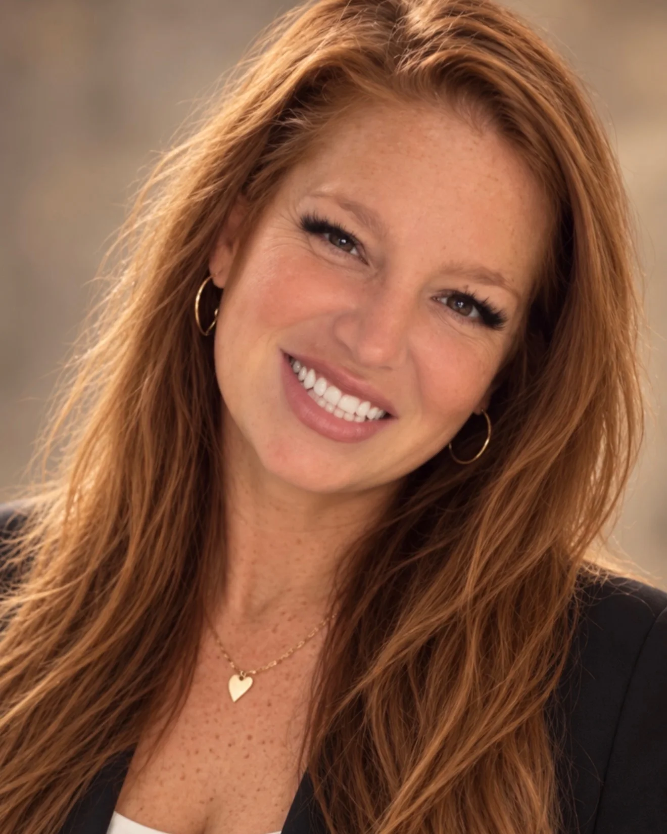 Lisa, owner of Lash L’Atelier, smiling in a black blazer with long auburn hair